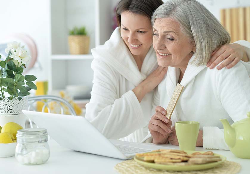 Senior women and daughter in a bathrobe smiling with laptop and tea